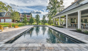 Rectangular fiberglass pool with dark finish and stone paver deck in a backyard with covered patio