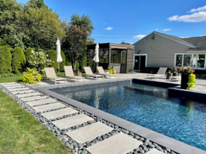 Modern gunite pool with dark finish, river rock stepping path, lounge chairs, and contemporary pergola in a backyard